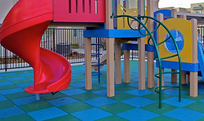 Playful EPDM wet pour flooring in blue and yellow beneath a children's play structure with a red slide