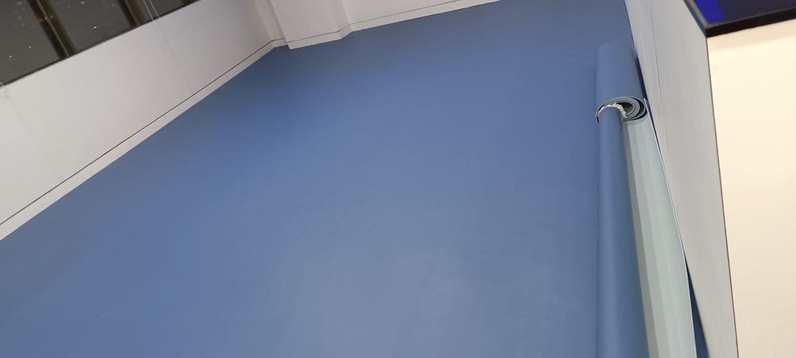 Blue PVC vinyl sports flooring along a hall wall with skirting