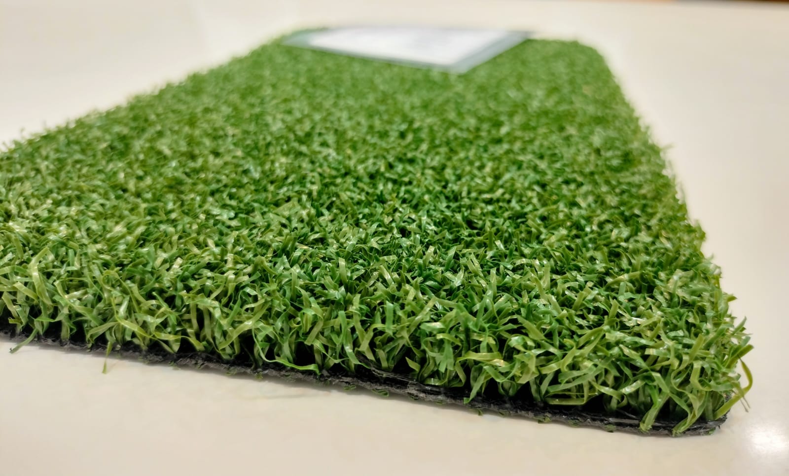Green multisports artificial grass sample showing pile and backing